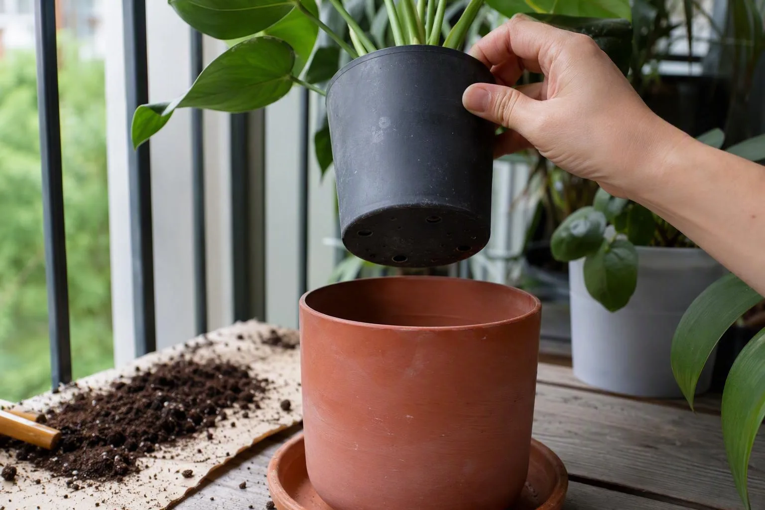 A hand lifts a plant pot to show its drainage openings above a terracotta cover pot on a balcony workbench.